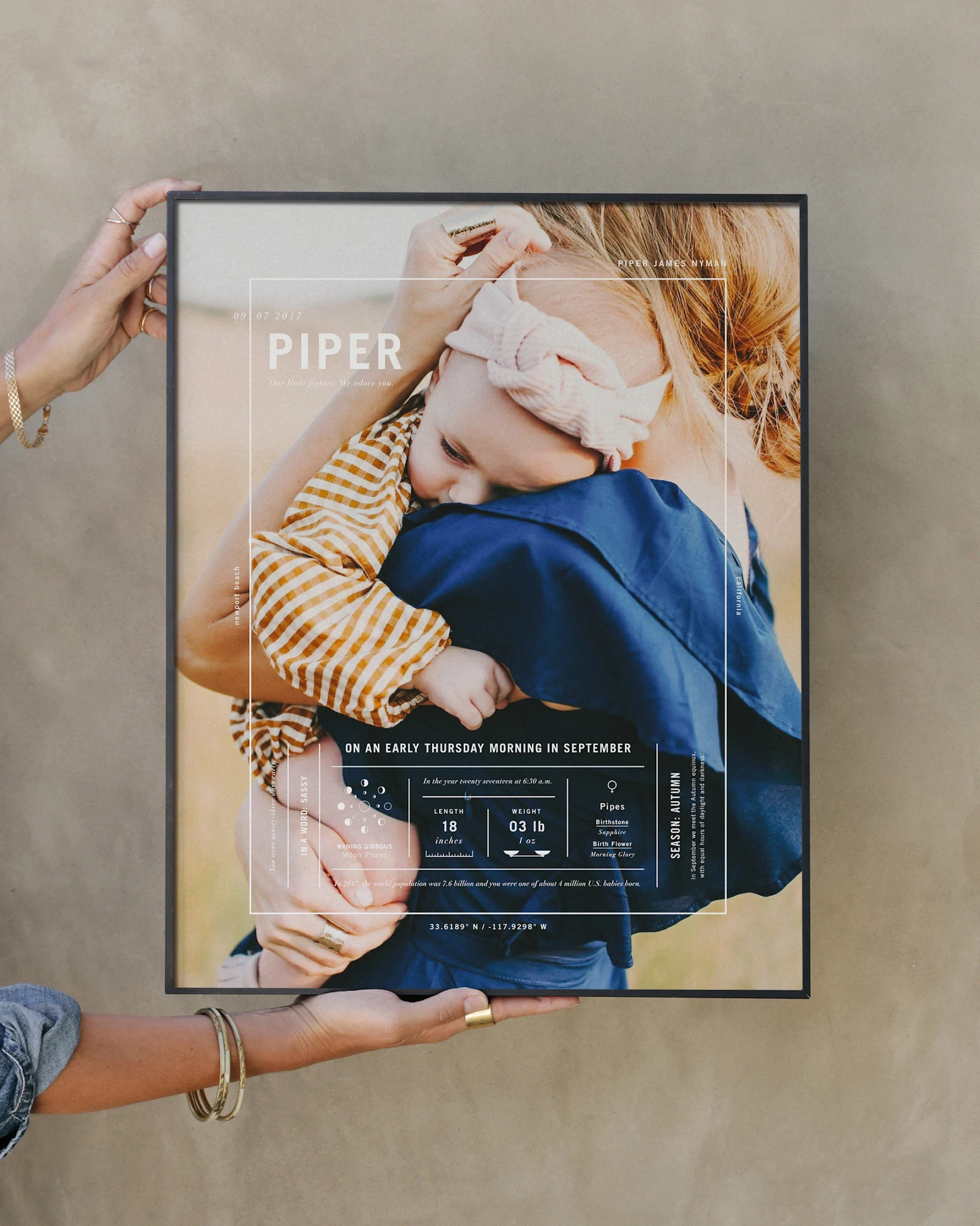 Hands hold a framed Birth Stat print with a sleeping baby photograph.