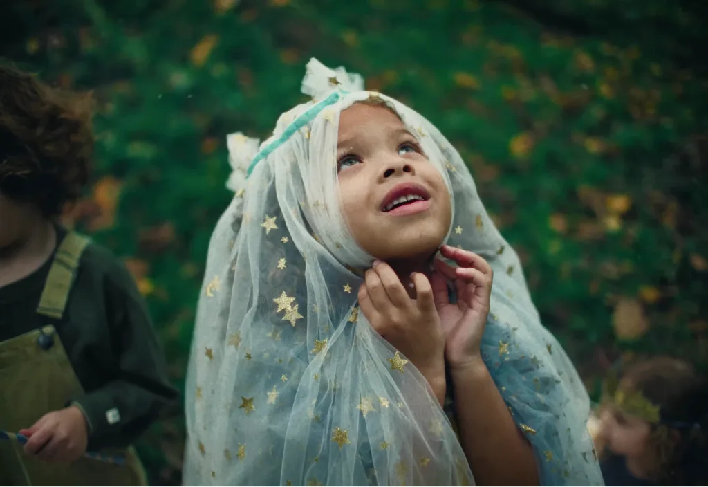 A child looks upward outdoors while wearing a translucent cloth patterned with gold stars.