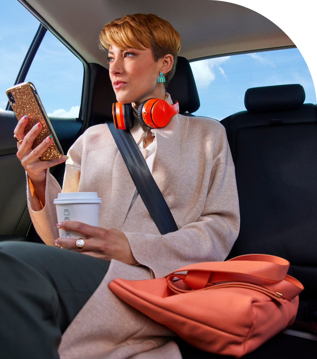 woman with bright headphones holding phone and coffee with bag in backseat of car