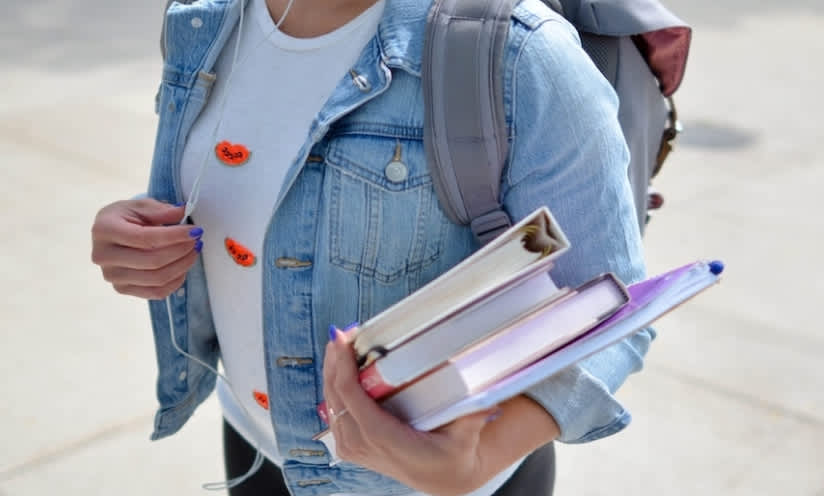 college student with backpack headphones carrying books 