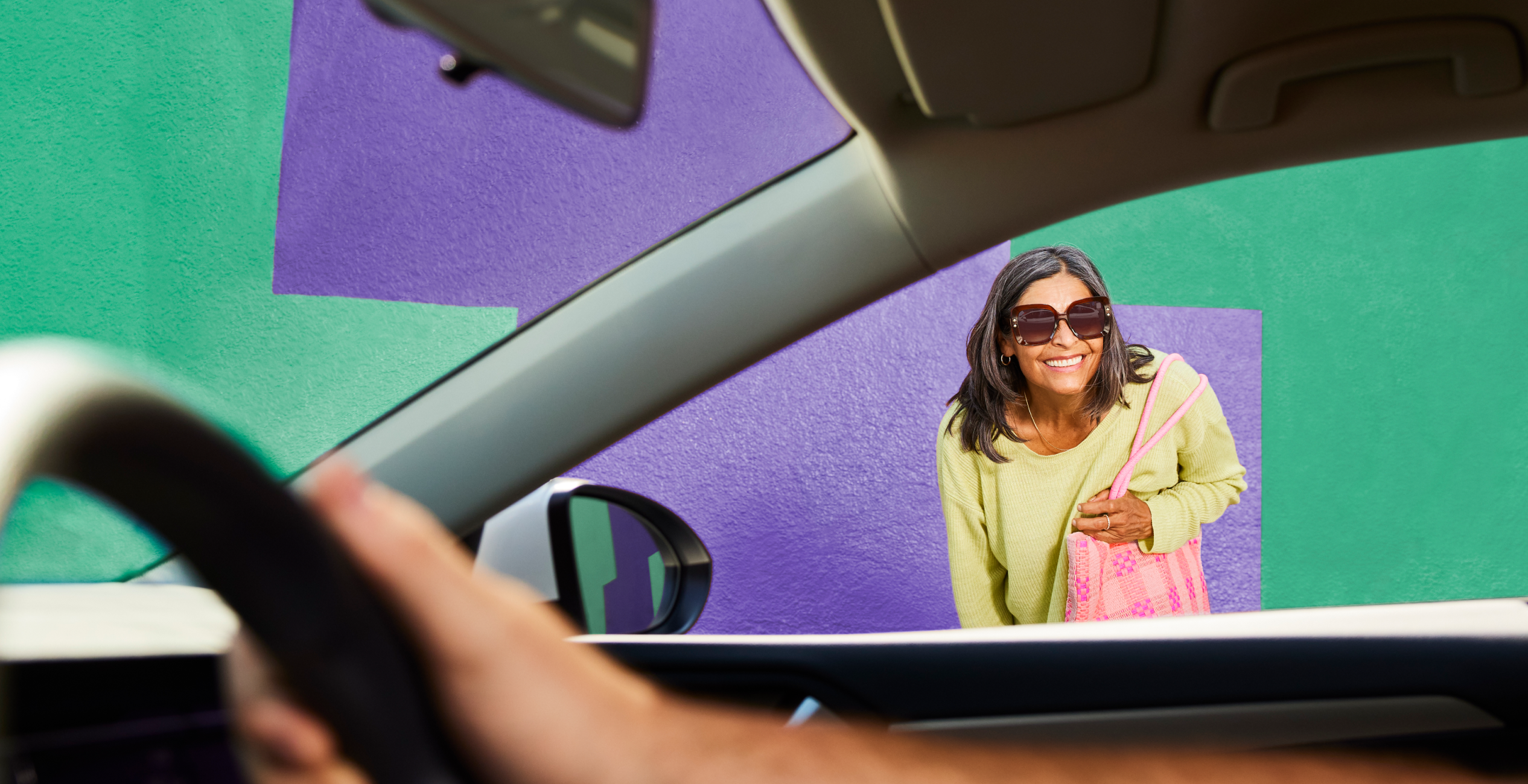 woman in sunglasses with pink purse looking into car with hand on steering wheel