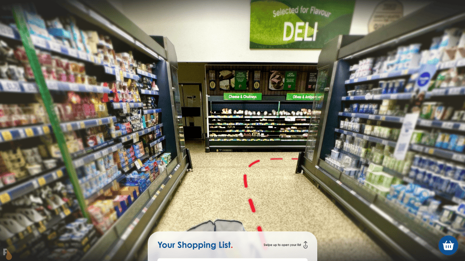 First-person view inside a grocery store with an augmented reality navigation path marked by red arrows on the floor, as seen through Apple Vision Pro AR glasses, with a minimized shopping list tab at the bottom of the view.