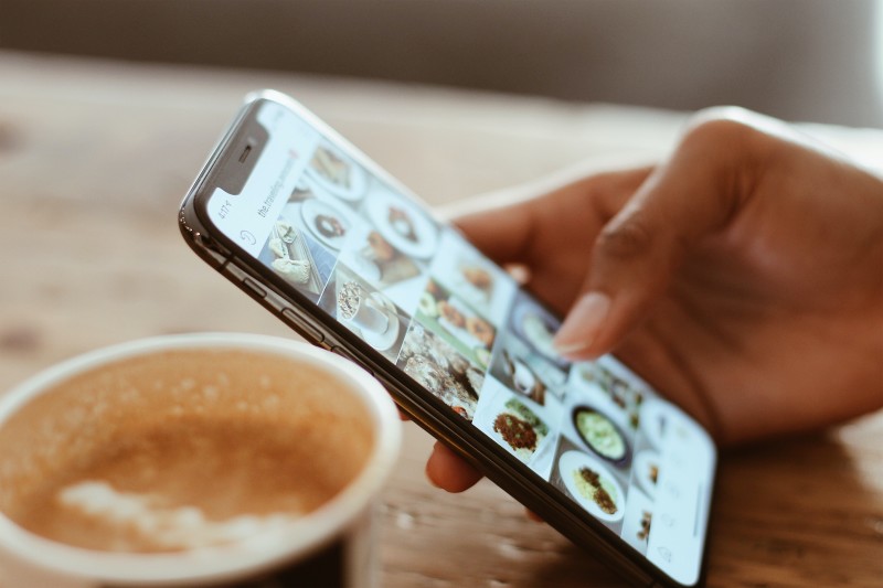 Closeup of a hand holding a cell phone next to a cup of coffee