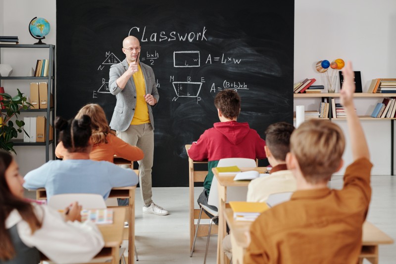 Photo of a classroom with a child raising their hand (Article Image)