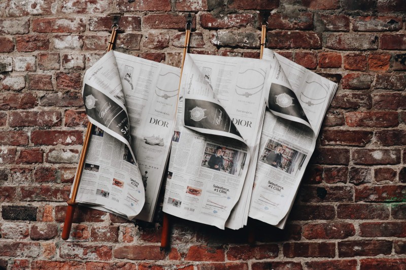 Three newspapers hanging on a brick wall