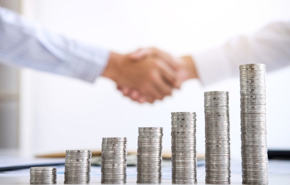 Business partners shake hands in front of a rising tower of coins