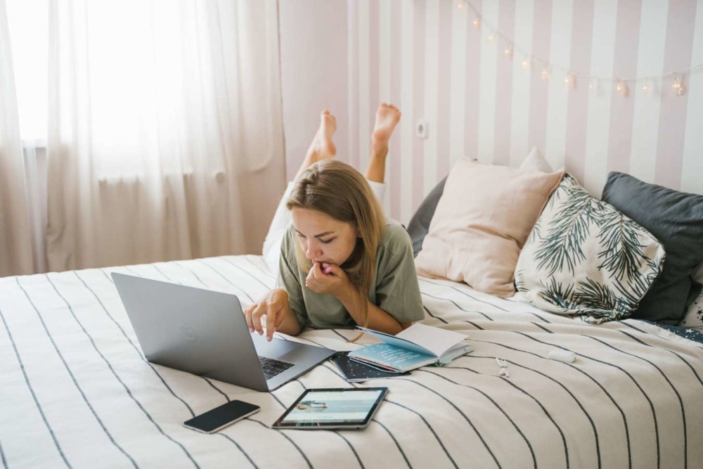 Woman on bed with open computer, phone, tablet, and open book