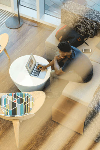 Looking down from above at a man sitting on a couch using his laptop.