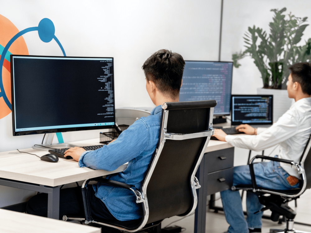software developers at desk programming with multiple monitors