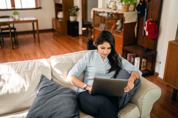 Woman on couch looking at laptop or tablet. She appears to be working from home. 