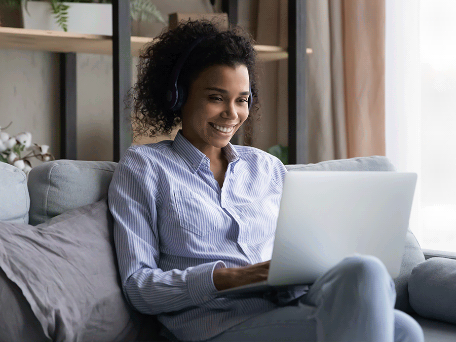 Woman in headphones working on laptop computer from a couch