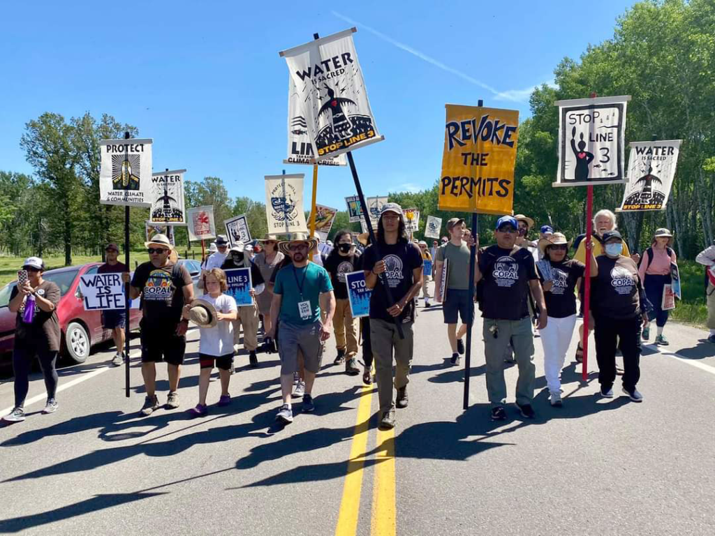 A group of people holding signs to protest Line 3