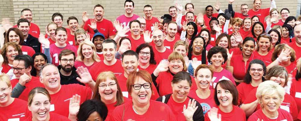 Large group of people wearing red shirts waving at the camera