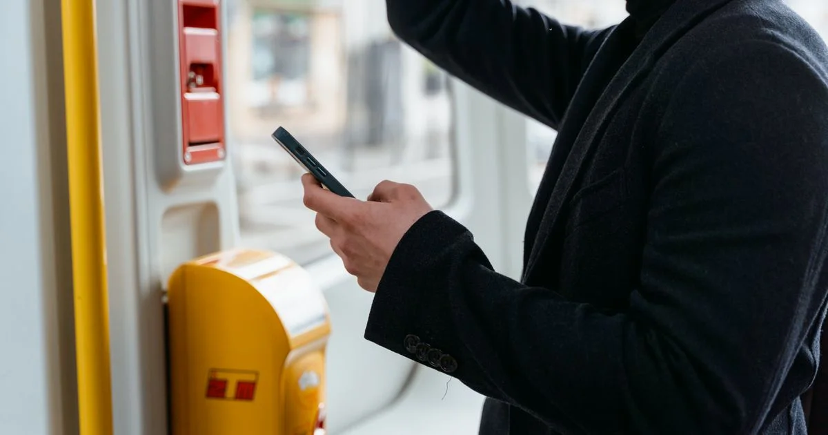 A traveller in a dark coat checks travel updates on a smartphone during a journey.  (source: https://images.pexels.com/photos/7251087/pexels-photo-7251087.jpeg)