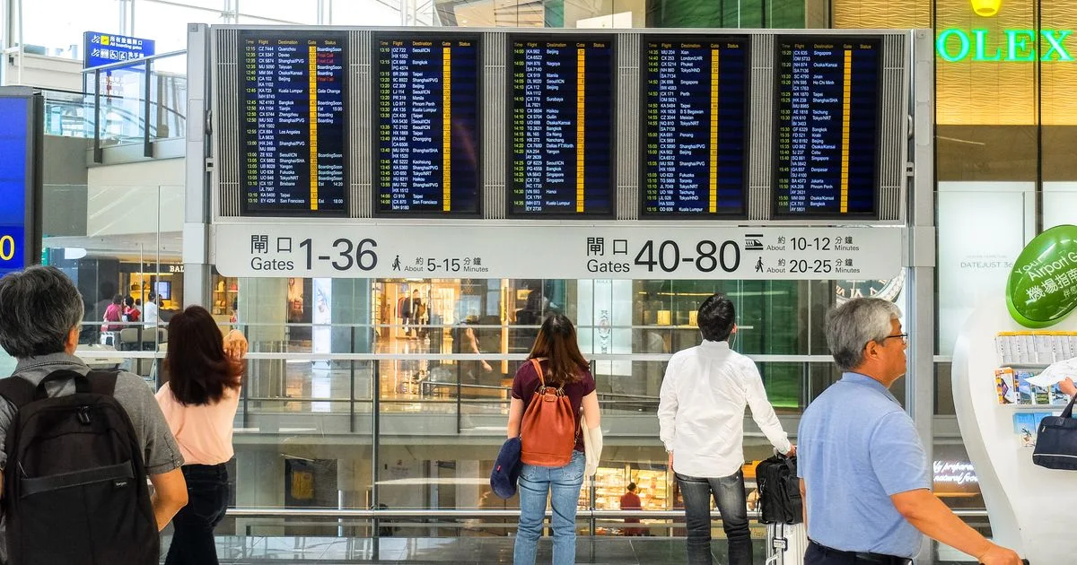 Passengers standing beneath a large digital flight-departure board in an airport hall.  (source: https://images.pexels.com/photos/12717154/pexels-photo-12717154.jpeg)