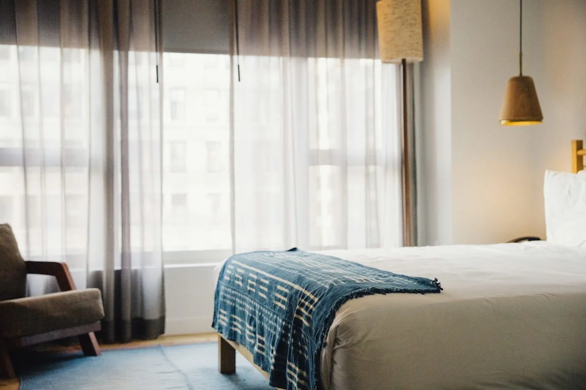 A comfortable hotel room with a bed, chair and window, typical of a managed business-travel stay.  (source: https://images.unsplash.com/photo-1702255489644-392758161f1f)
