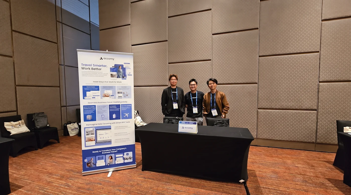 Three members of the Accomy team standing behind the exhibition table at their World AI Show Malaysia 2026 stand in Kuala Lumpur, beside a pull-up banner.