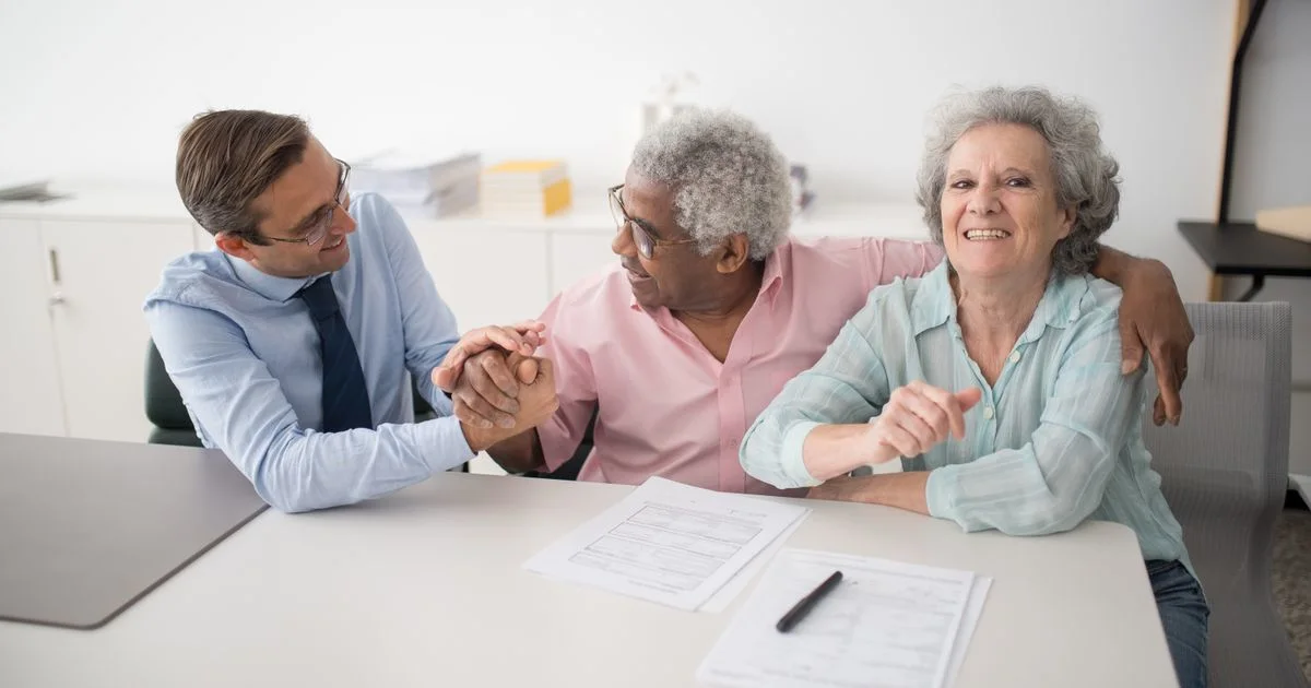A travel agent at a desk reviews documents with a smiling seated couple. (source: https://images.pexels.com/photos/8441861/pexels-photo-8441861.jpeg)