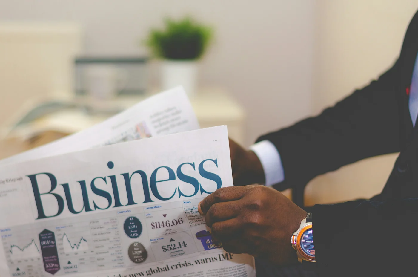 Person in a suit reading the business section of a newspaper showing financial figures
