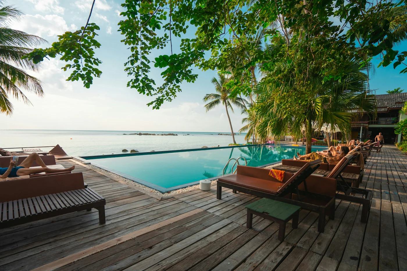 Infinity pool and wooden deck loungers framed by palms overlooking a calm tropical sea