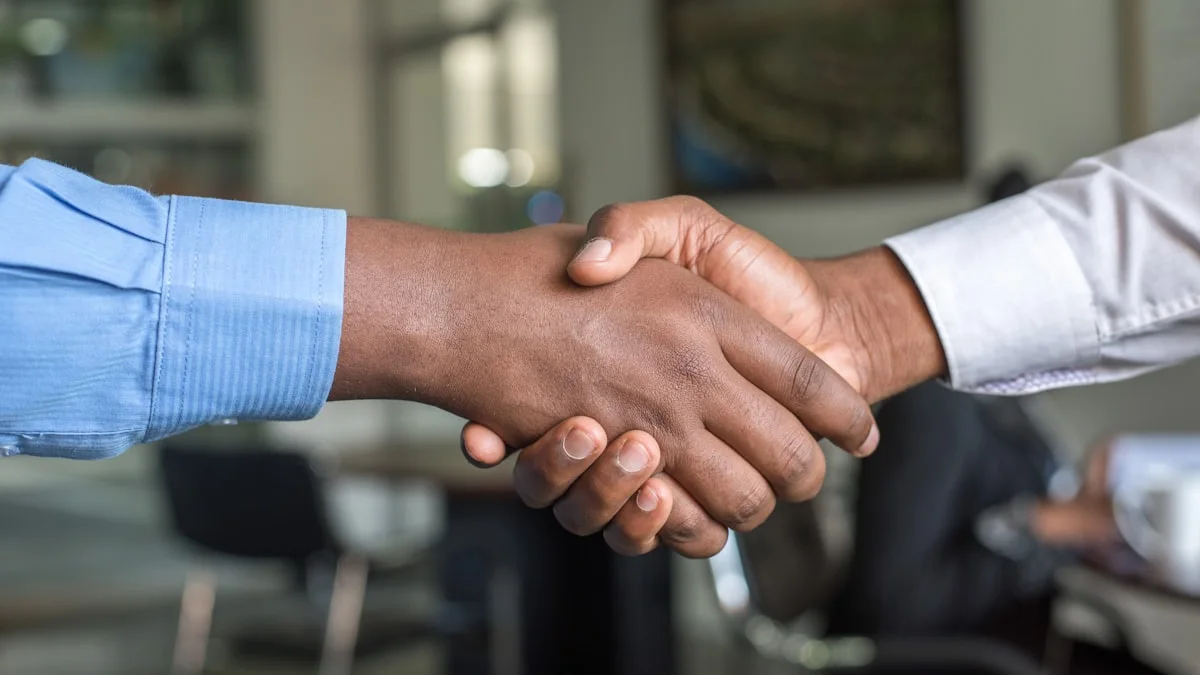 Two people shaking hands over a desk, signalling a policy agreement. (source: https://images.unsplash.com/photo-1521791136064-7986c2920216)