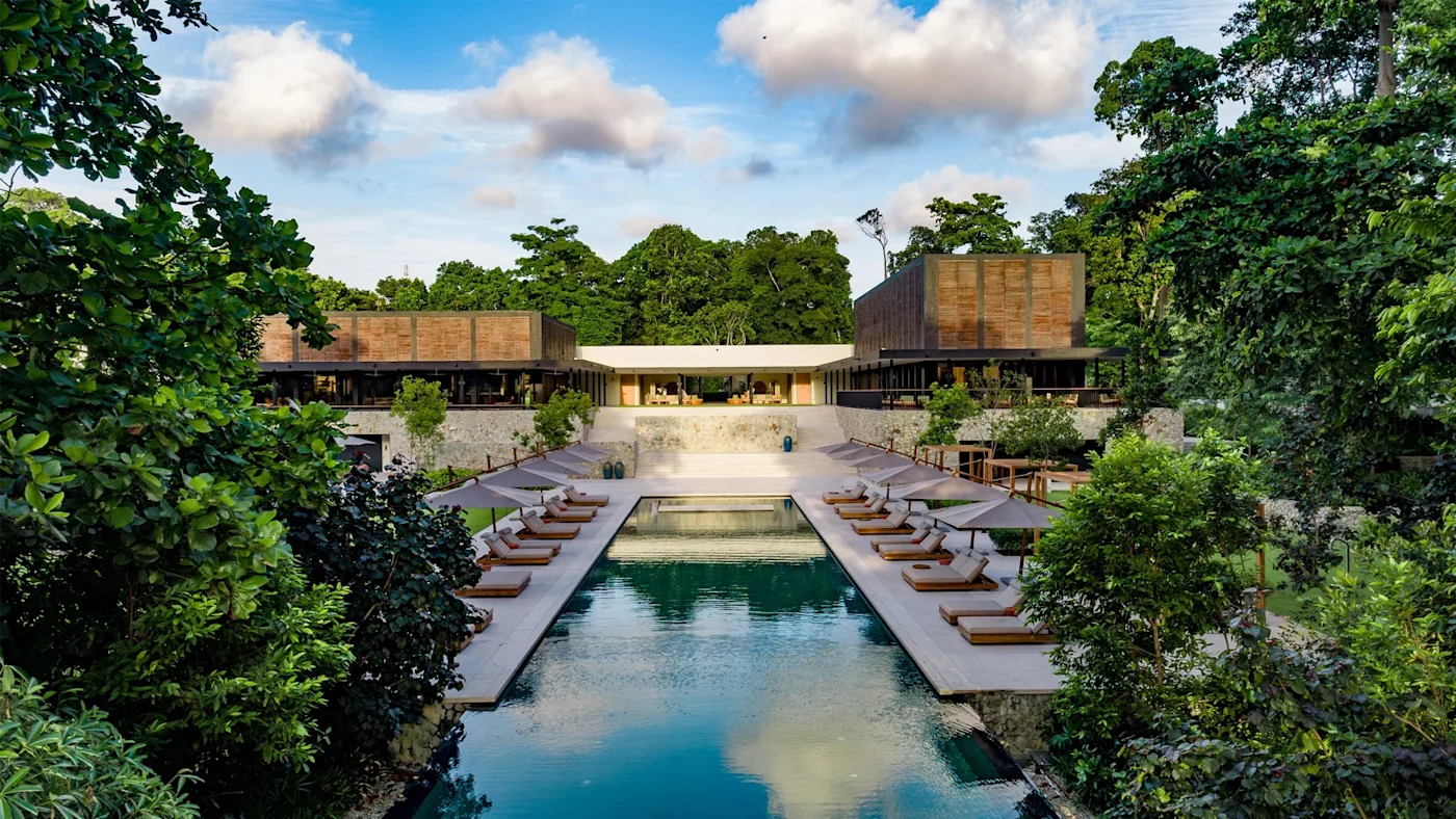 Low timber-screened pavilions around an axial pool, set into rainforest on the Johor coast.