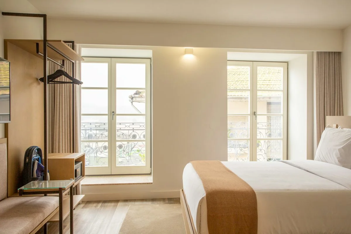 A large, well-appointed hotel room with a king bed beside a bright window.  (source: https://images.unsplash.com/photo-1702014861736-d62834317c5e)