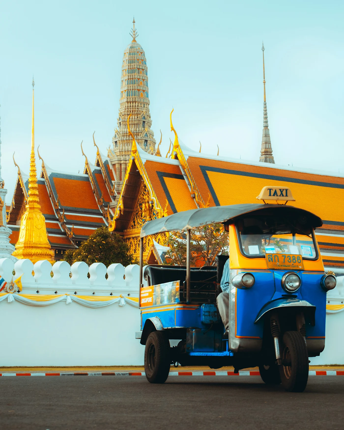 Blue and yellow tuk-tuk taxi parked before the golden spires of an ornate Bangkok temple