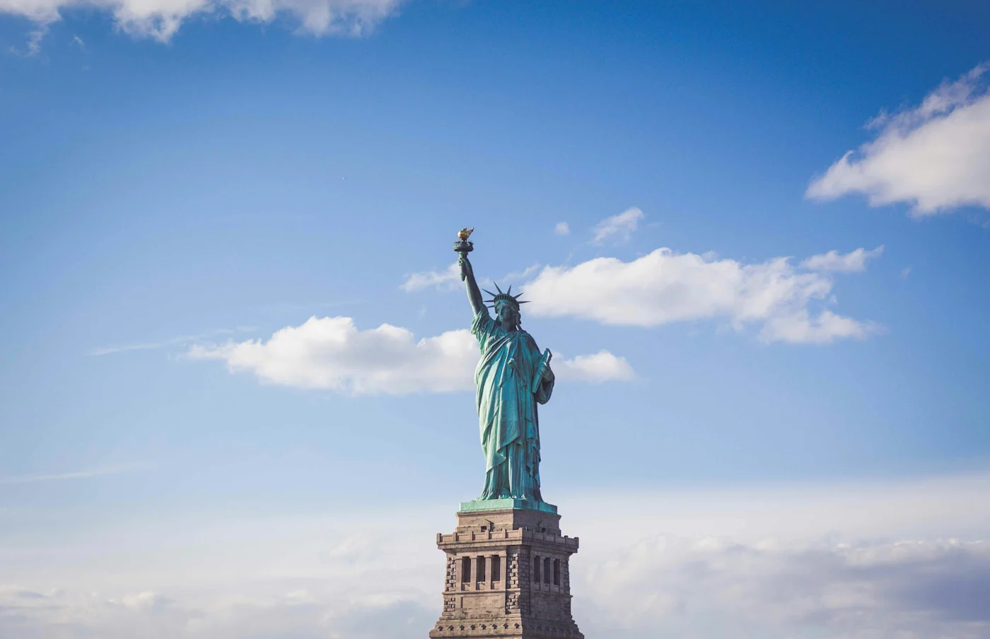 The Statue of Liberty on its stone pedestal against a bright blue sky with scattered clouds