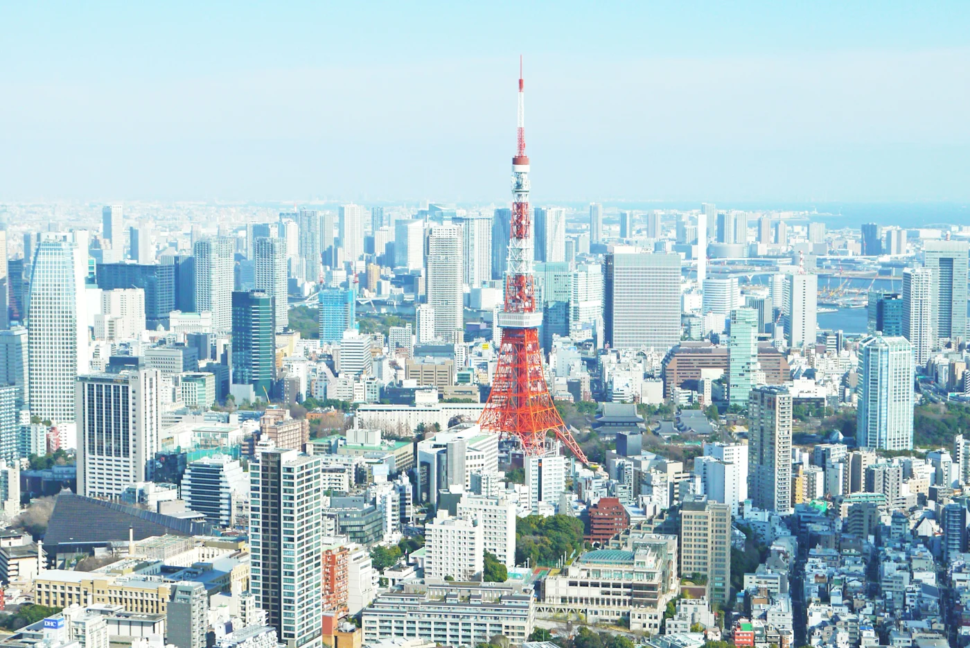 The red-and-white Tokyo Tower rising above a sprawling Tokyo cityscape under a pale blue sky