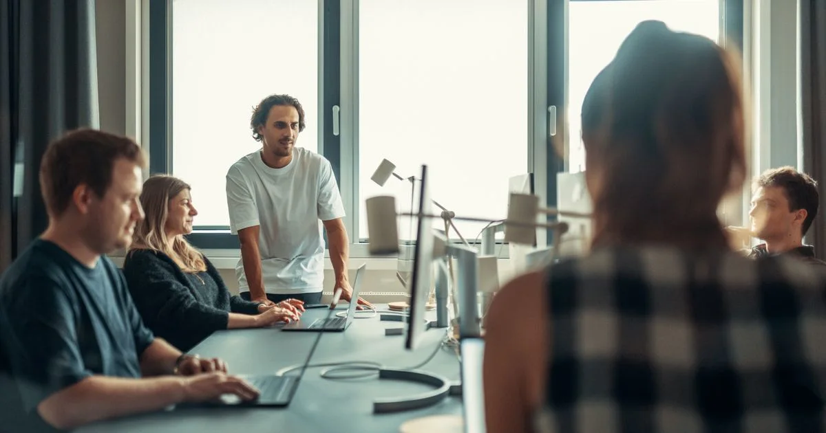 Diverse colleagues in business-casual attire discussing around a table in a bright, modern office.  (source: https://images.pexels.com/photos/32082430/pexels-photo-32082430.jpeg)