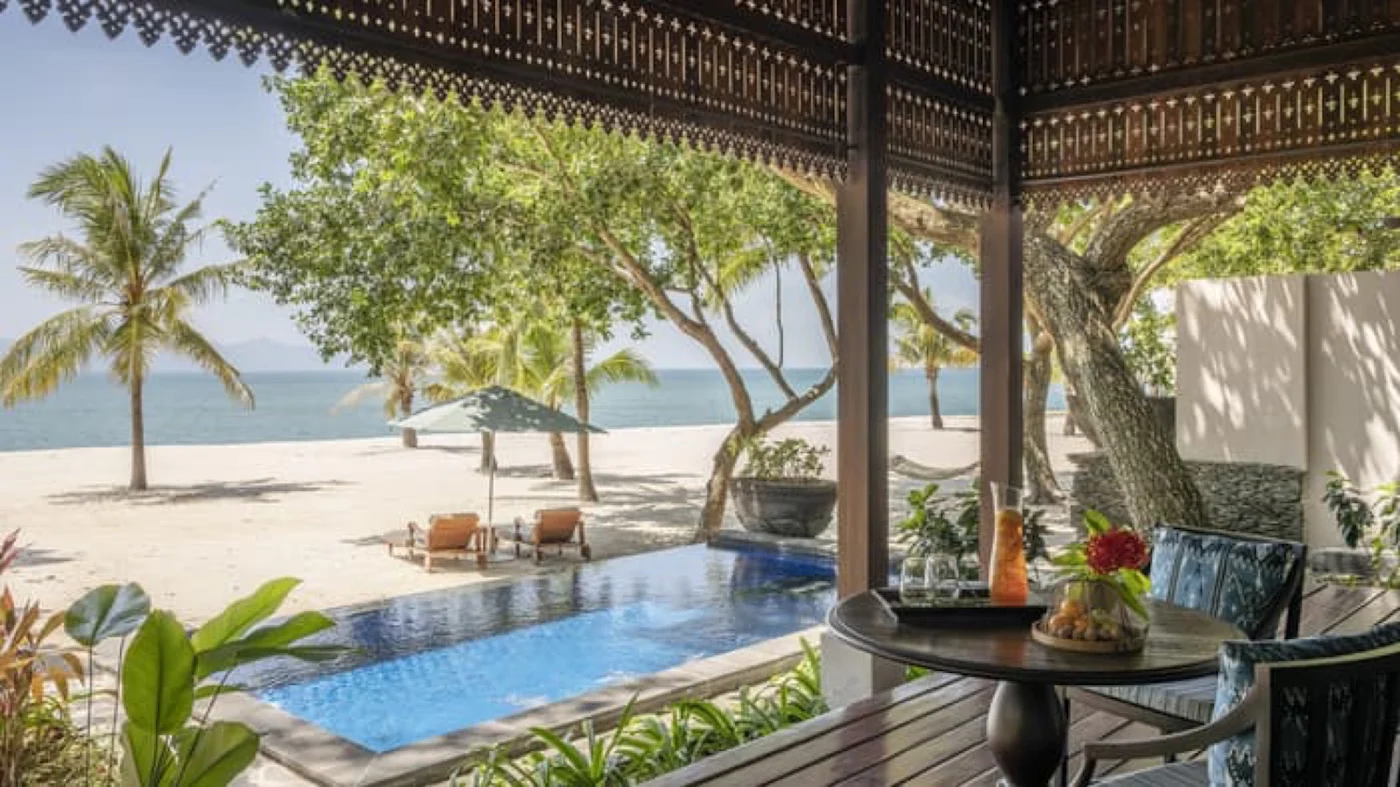 A beach pavilion villa with a private pool, looking out through carved timber fretwork to the Andaman Sea.