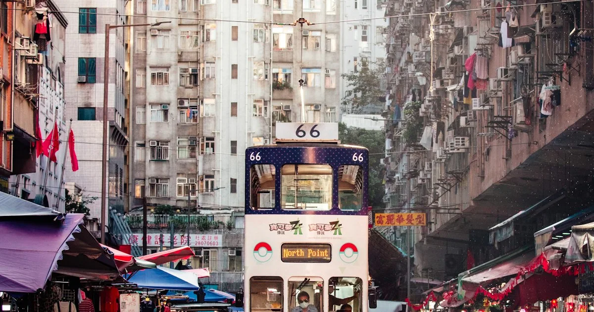 A double-decker tram threading a busy Hong Kong street lined with shops and market stalls.  (source: https://images.unsplash.com/photo-1760205469248-d762bd55304b)