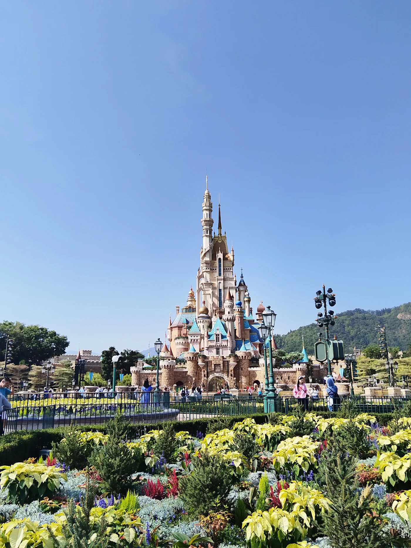The fairytale castle at Hong Kong Disneyland behind colourful flower gardens under a clear blue sky
