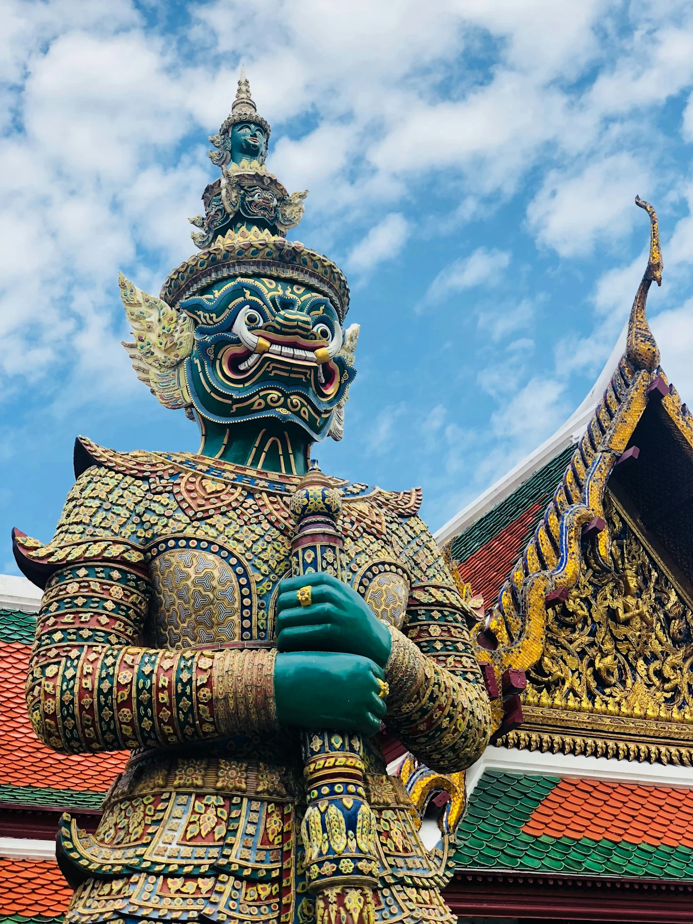 Ornate green Yaksha demon guardian statue beside a gilded temple roof at Bangkok's Grand Palace