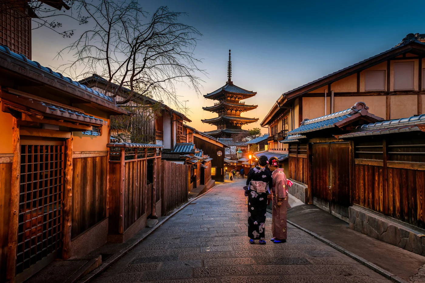 Two women in kimonos on a historic Kyoto street at dusk with the Yasaka Pagoda behind