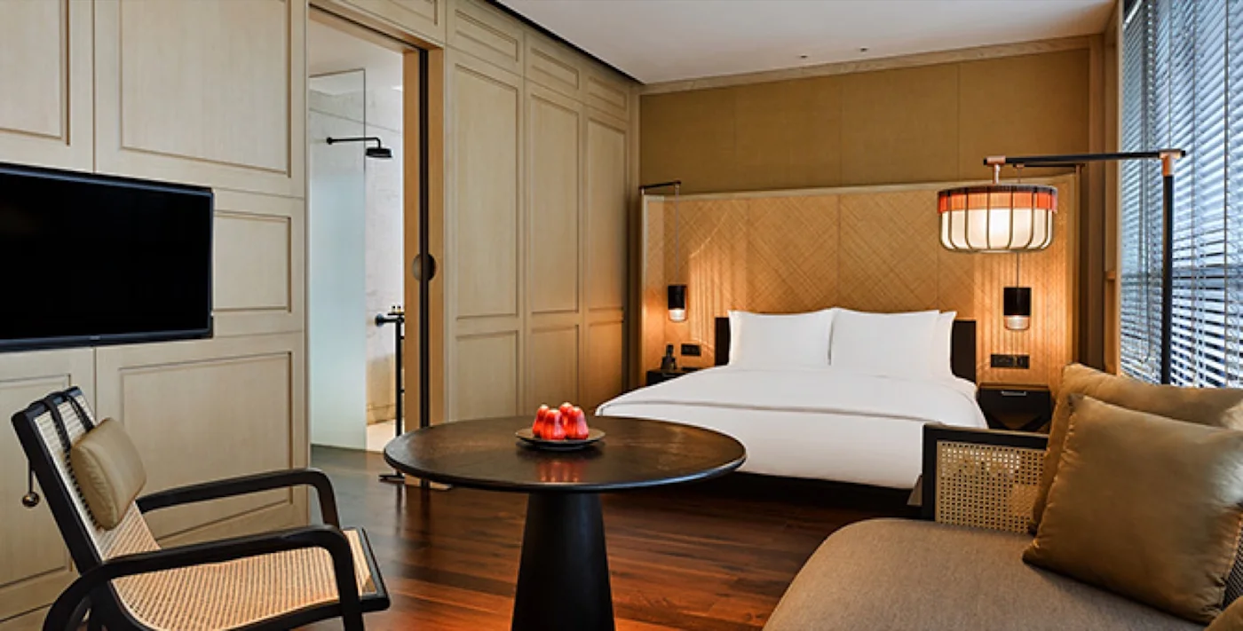 A guestroom with woven kelarai panelling behind the bed, rattan seating and brass fittings.