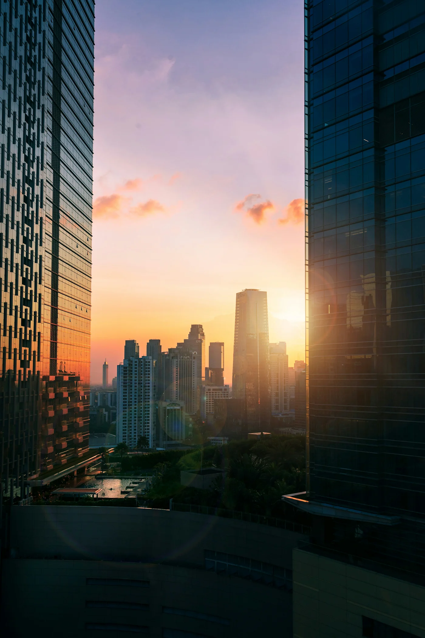 Sun setting over a city skyline framed between two glass skyscrapers