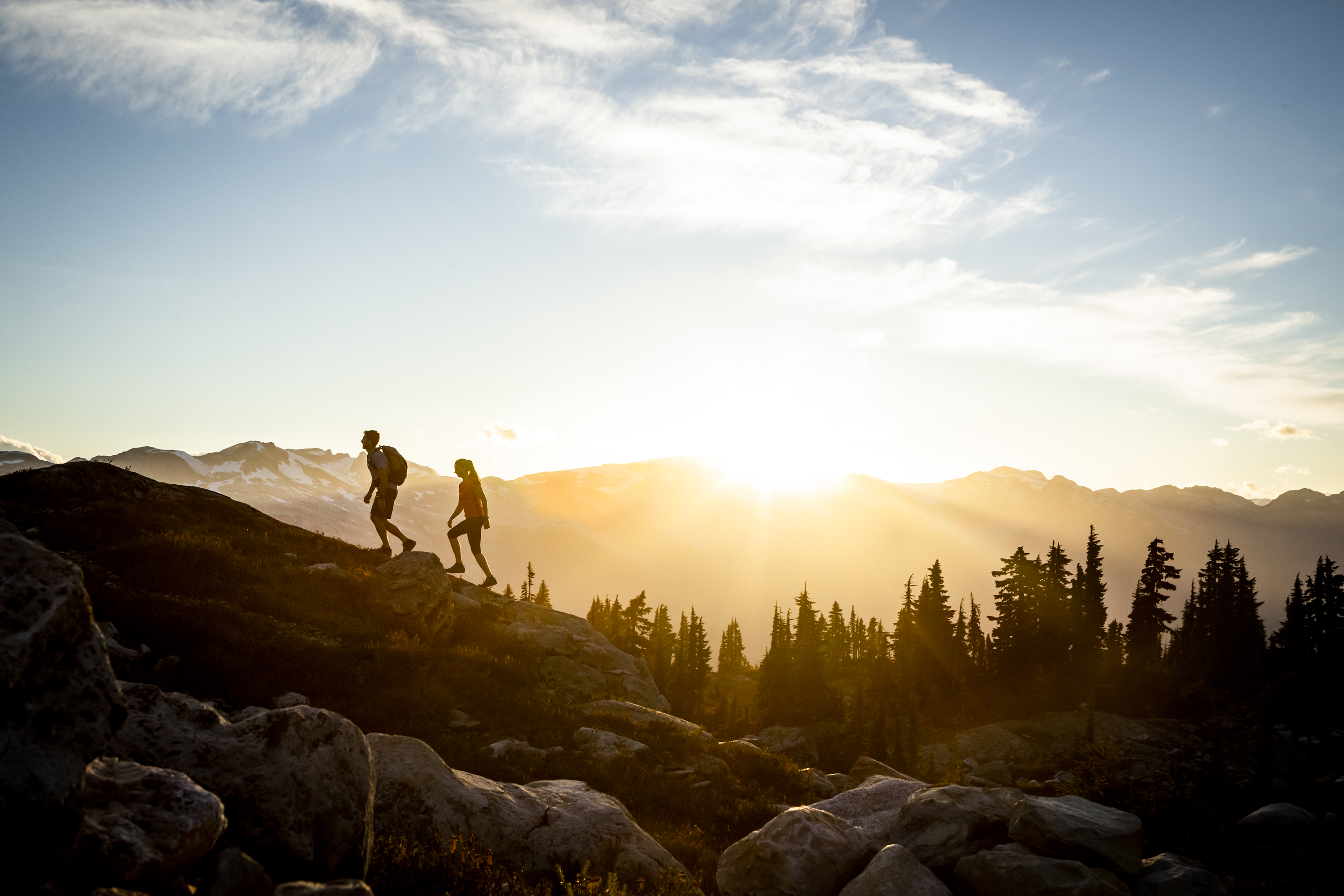 Two people hiking on a mountain with the sun setting.