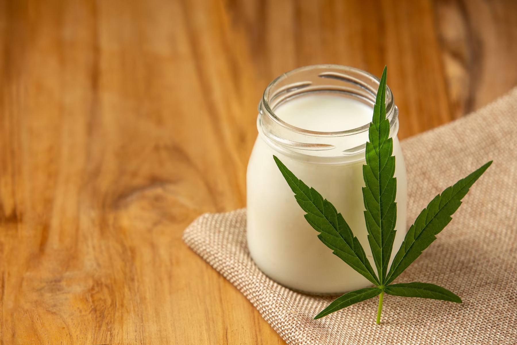 Image of glass of hemp milk with hemp leaf laid on it