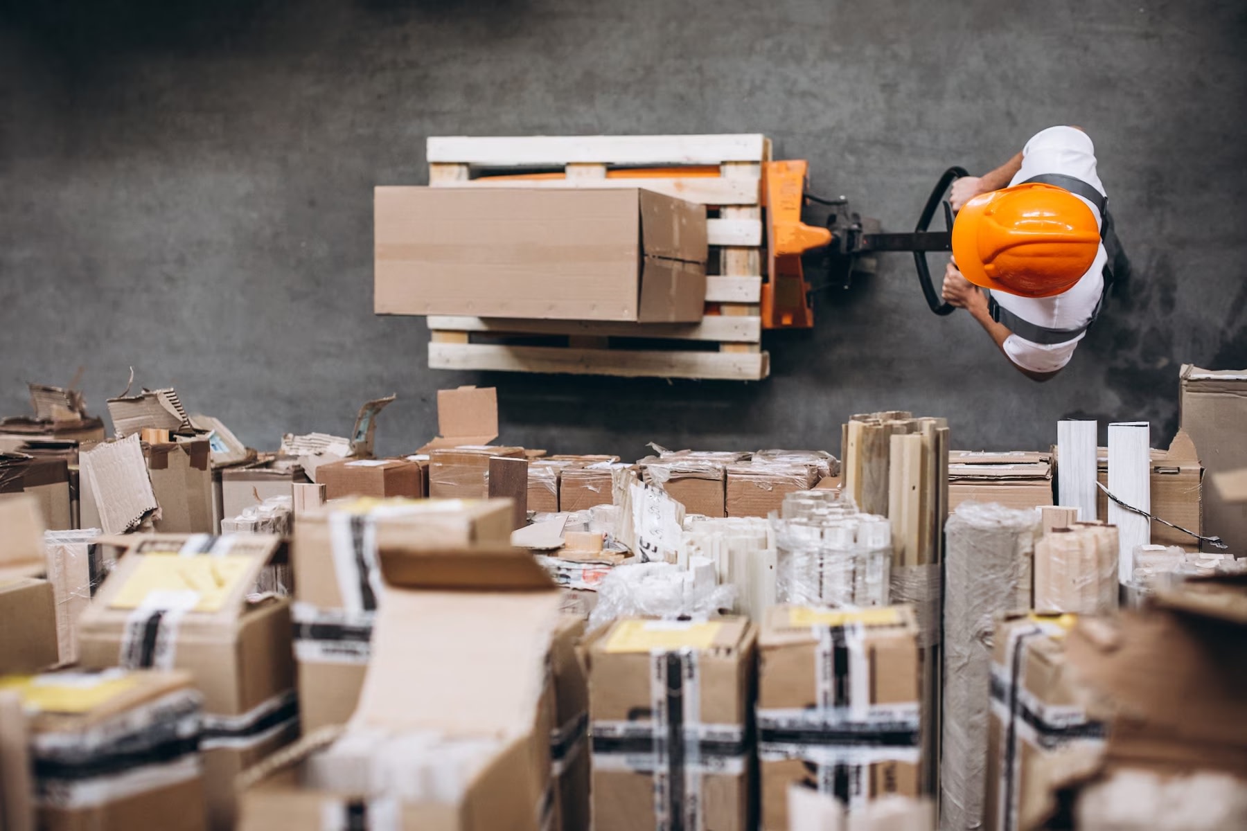 Image from above of man pushing cart in warehouse full of packaging
