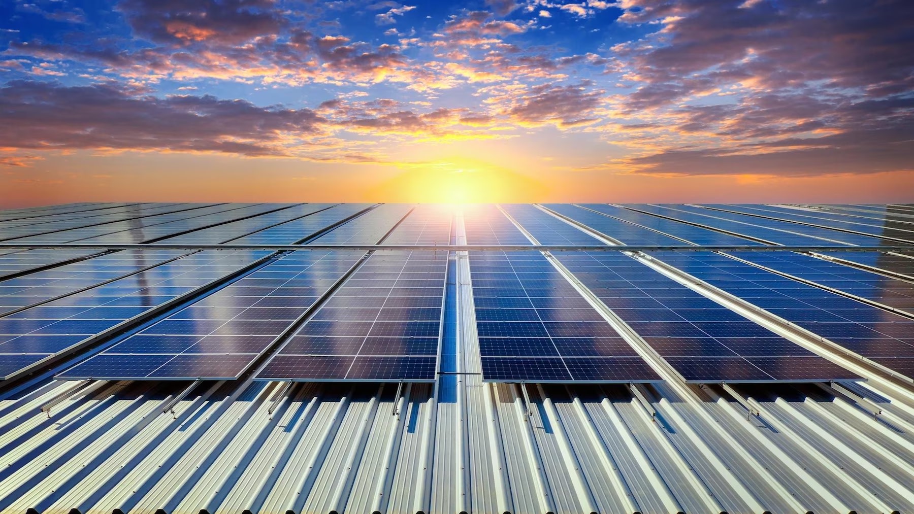 Image of solar PV panels on rooftop with background of clouds and sunset