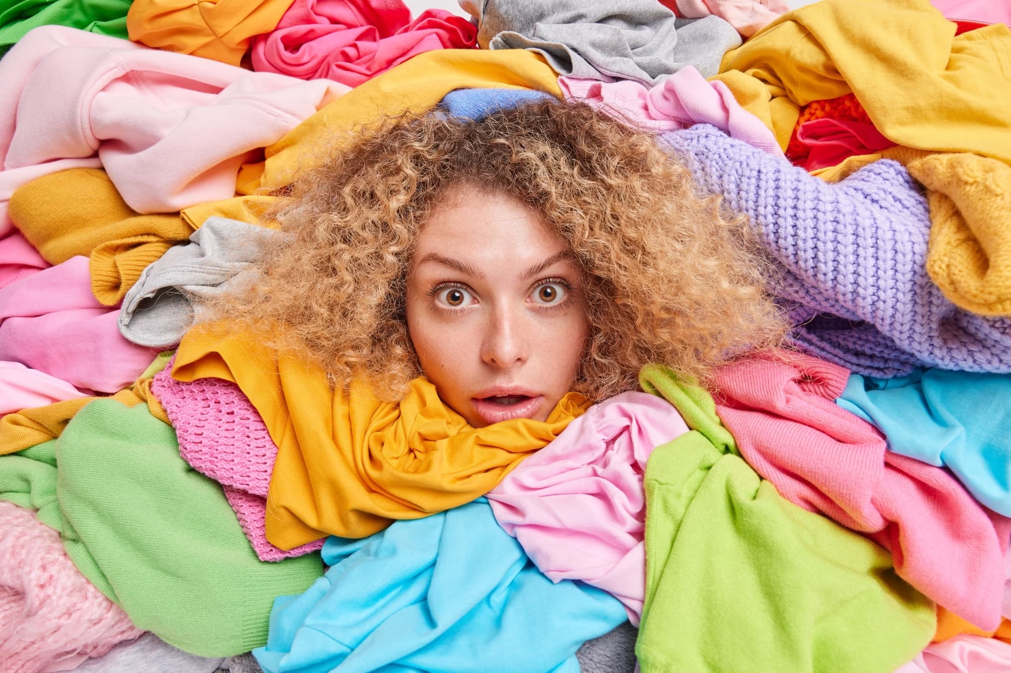 Image of woman's head peeking through assorted pile of clothing