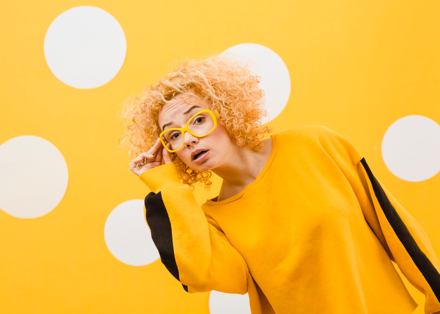 Image of pretty blonde woman wearing yellow, with yellow glasses, on yellow and white polka dot background