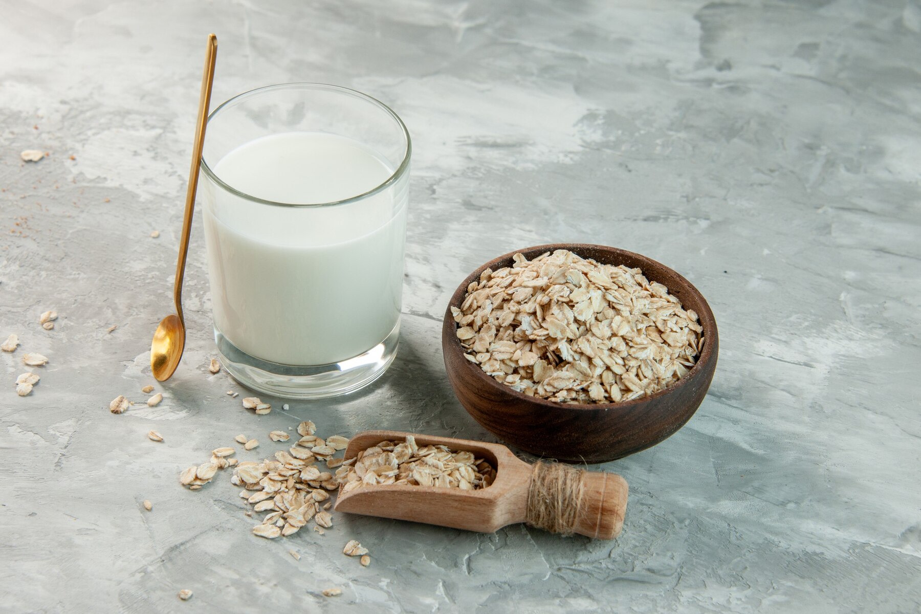 Image of glass filled with oat milk and bowl and scoop of whole oats
