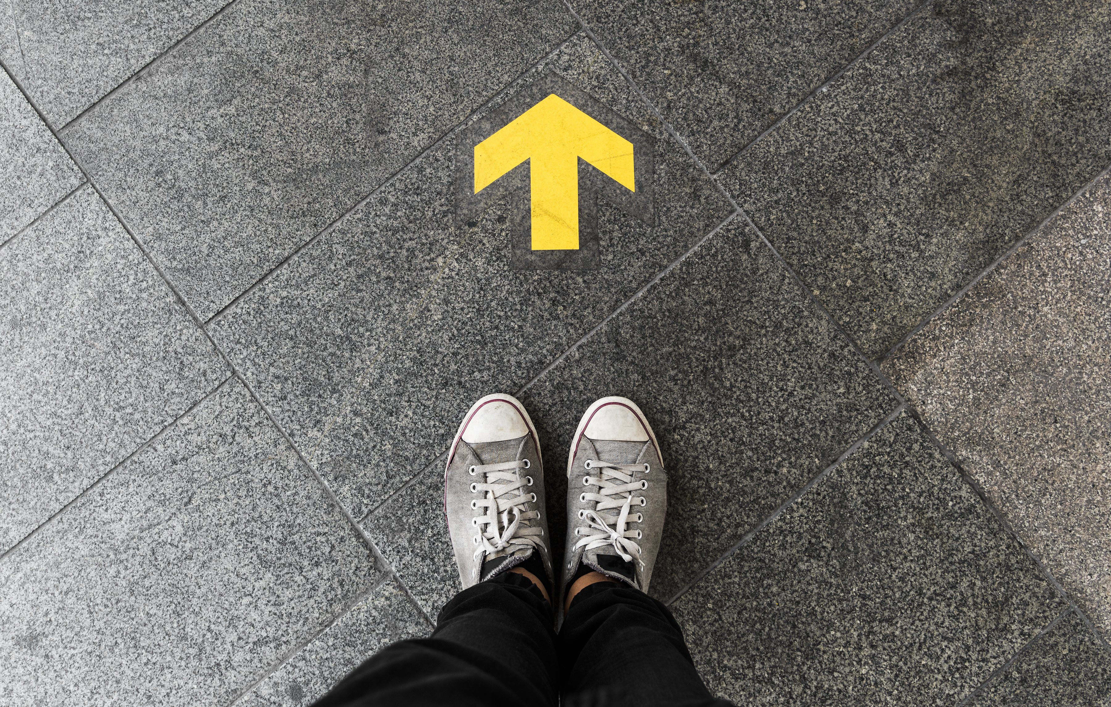 Image looking down at shoes (feet) with a yellow arrow pointing forwards and away