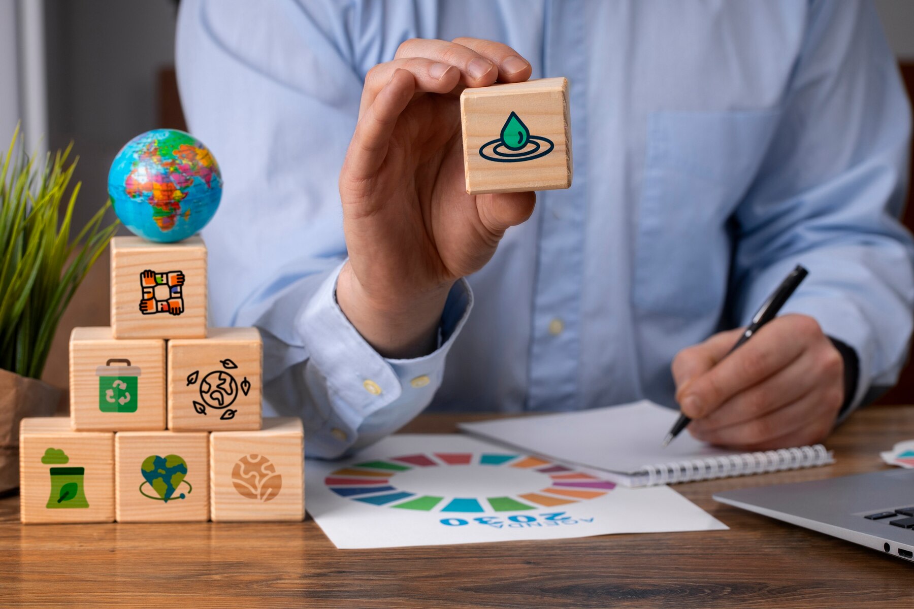 Image of businessman at desk holding wooden ESG cube, next to pyramid of similar cubes and a globe of the Earth
