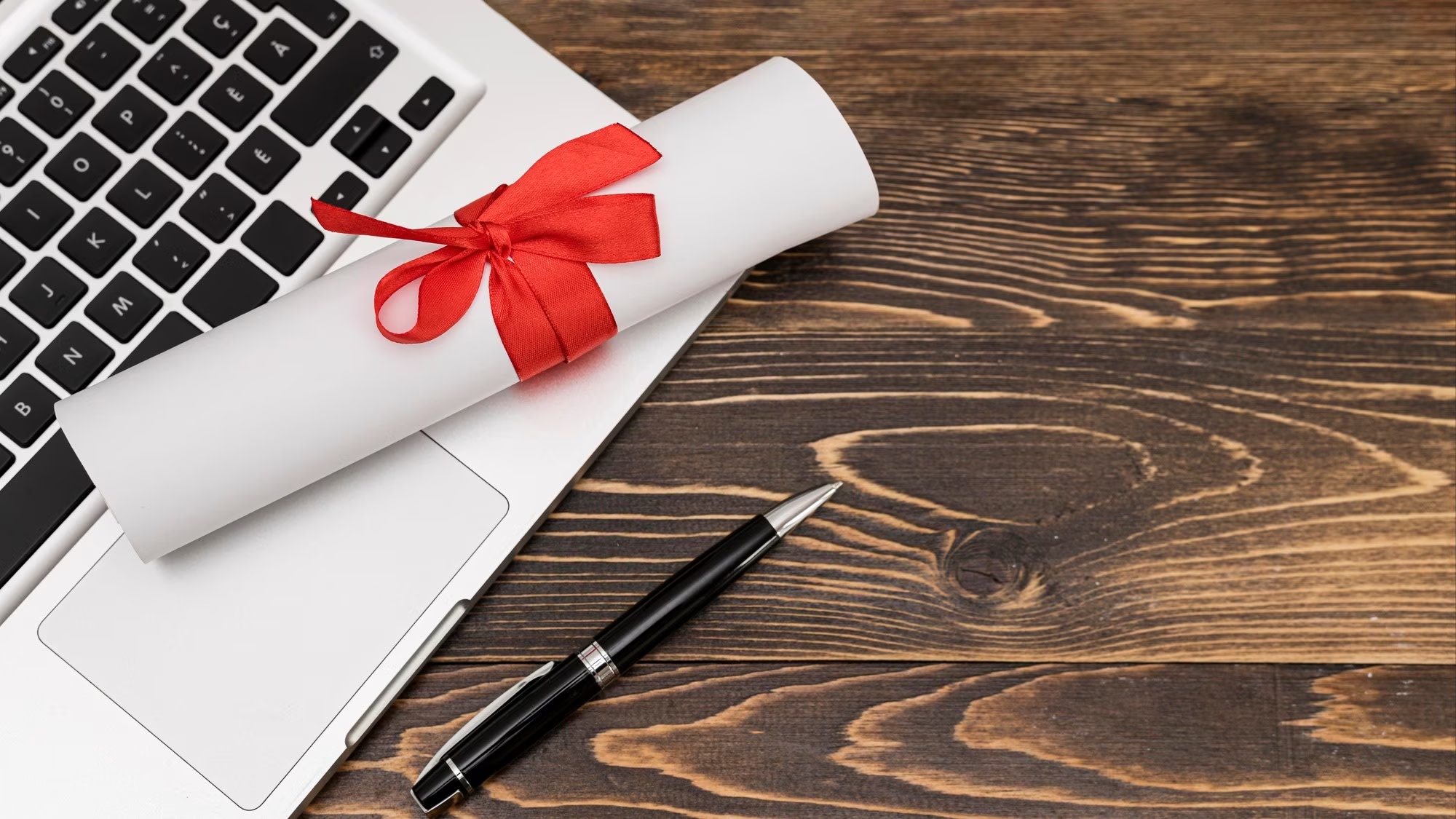 Image of graduation diploma and ribbon on laptop on wooden table