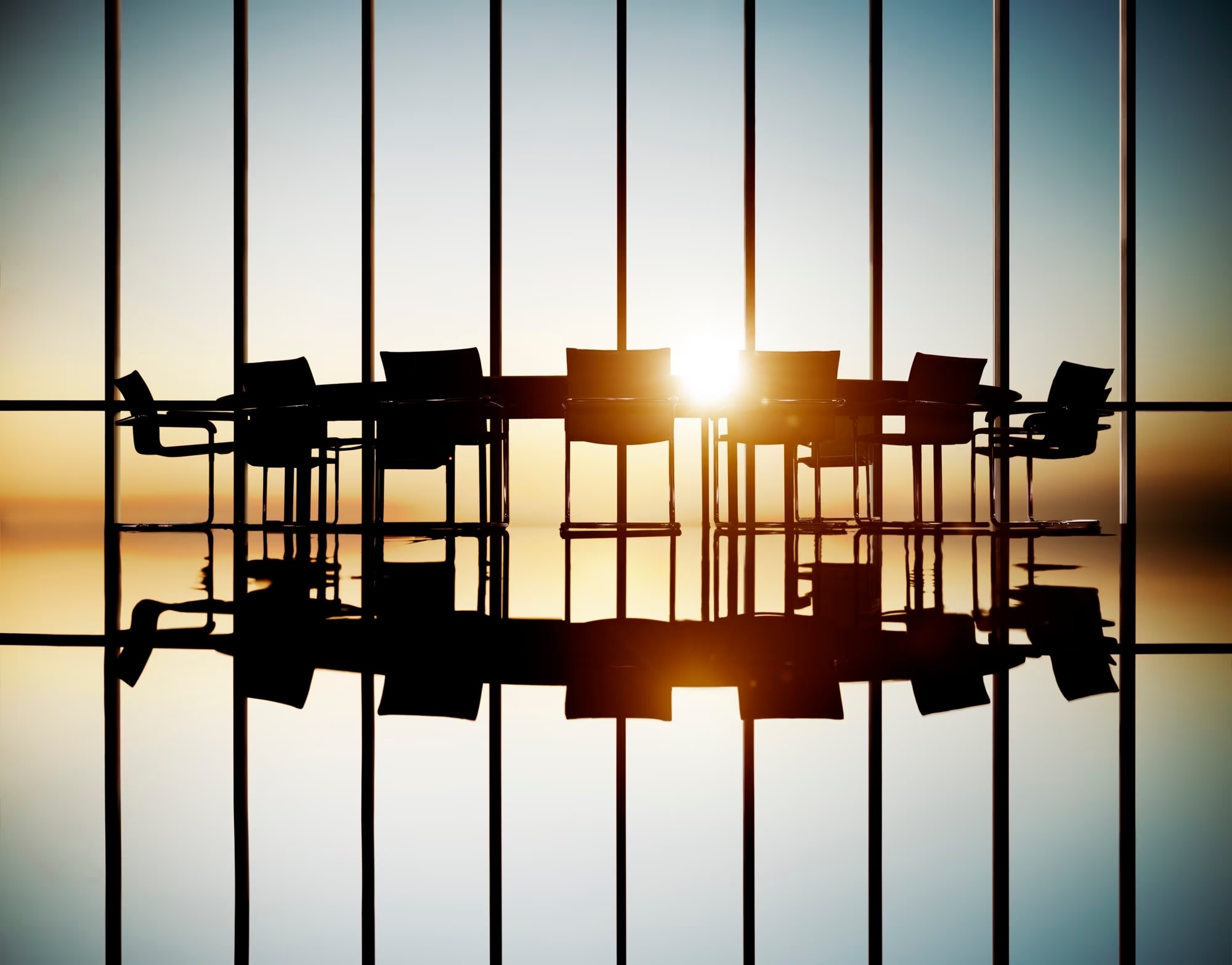 Image of meeting room chairs and table with floor-to-ceiling windows and view of sunset or sunrise