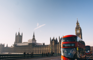 London red bus going across bridge with houses of parliament in background